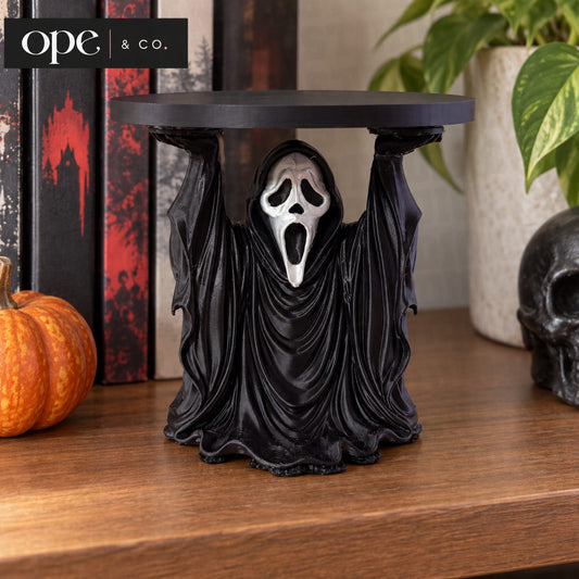 Black hooded ghost candle holder stand on a mantle with pumpkins and books